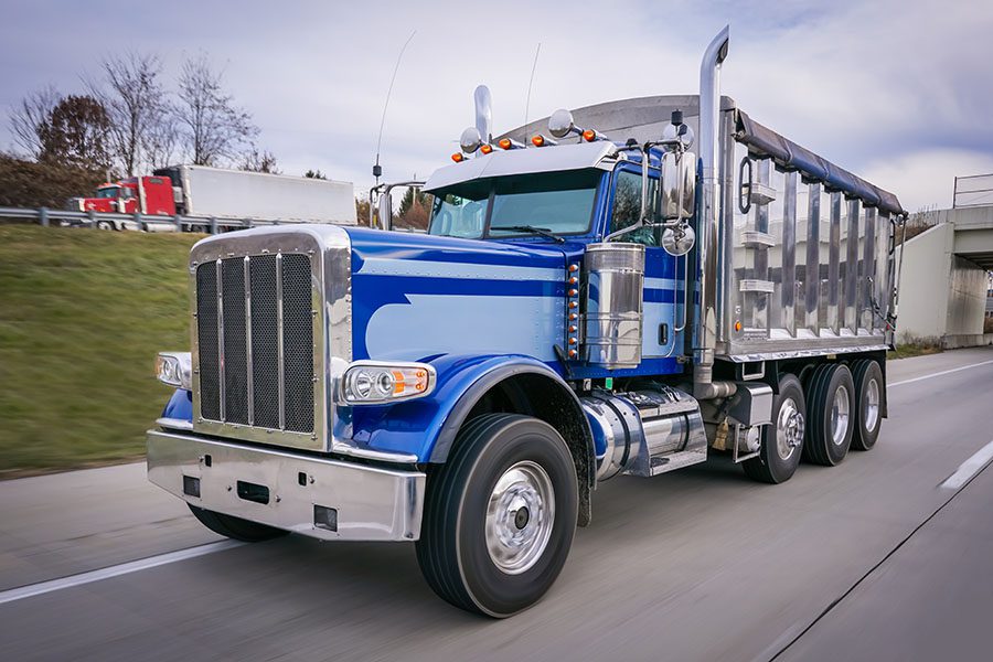 Meet Our Team - View of a Shiny Blue Dump Truck Driving on a Highway
