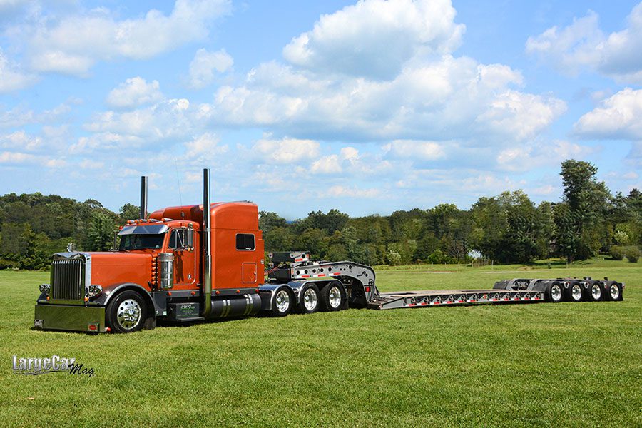 Specialized Business - View of a Red Semi Truck with a Tractor Trailer Parked on Green Grass Against a Blue Sky